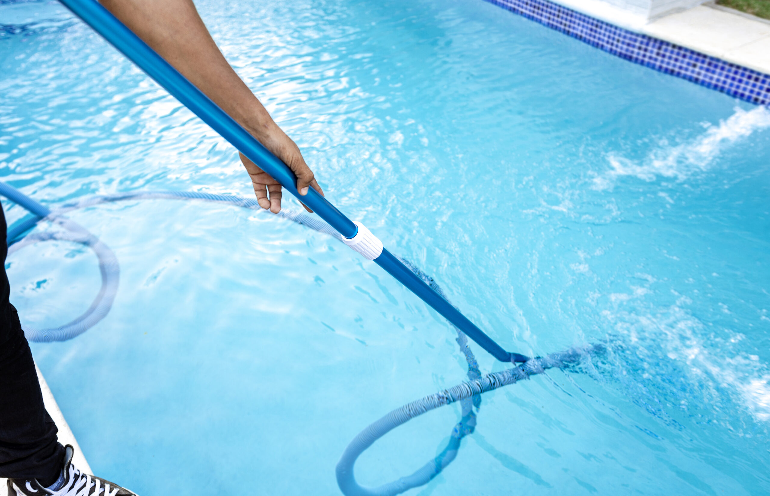 man cleaning a swimming pool with a vacuum hose
